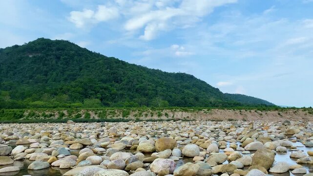 Boulders scattered in dry river alongside beautiful mountain with blue sky at Sylhet, Bangladesh.