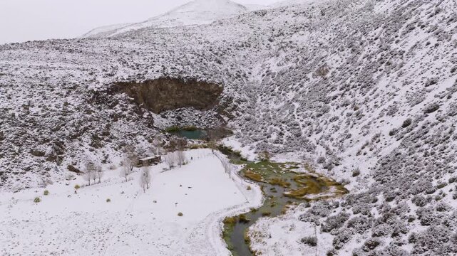 Laguna de la Ni&ntilde;a Encantada crater lake in Malarg&uuml;e Mendoza Argentina surrounded by snow covered volcanic terrain and winding stream in winter landscape drone sliding lateral panning