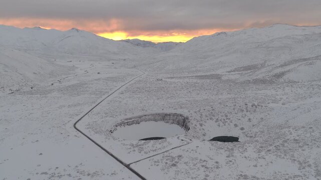 Pozo de las &Aacute;nimas twin sinkholes in Malarg&uuml;e Mendoza Argentina set in snow covered volcanic plateau with road and distant Andes glowing at sunrise, smooth drone pullback shot