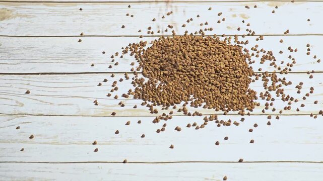 Brown seeds scattered on a rustic wooden surface. The seeds vary in size and shape, creating a natural, organic appearance.