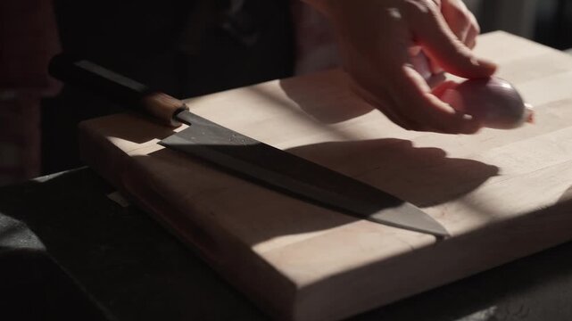A Japanese chef's knife is lifting off a sun soaked cutting board to prepare a shallot (slow motion 4K).