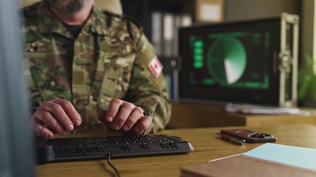 Canadian army officer typing on computer in office, planning defense strategies