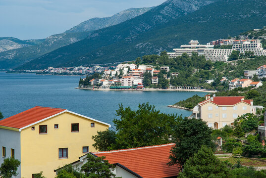 Scenic coastal town nestled between lush green hills and calm blue waters, featuring colorful houses, waterfront promenade, and modern buildings on hillside. Neum Bosnia-Herzegovina - June 5, 2007