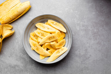Top view of slices of ripe plantains in a grey bowl, macro shot of slices of yellow plantains for frying on a grey countertop, process for making fried plantain © this_baker