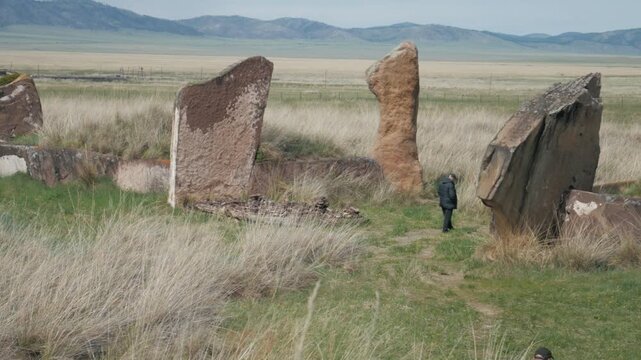 A man walks among the ancient standing stones of the Great Salbyk Kurgan in the Valley of the Kings, Khakassia. Handheld static shot capturing the historical archaeological site in the Siberian steppe
