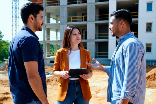Young adult business team discussing construction project on site, reviewing clipboard and coordinating workflow. Useful for real estate development, engineering, planning, teamwork marketing