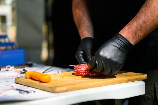 Close-up of a chef in black nitrile gloves precisely trimming a thick-cut ribeye steak with a sharp knife on a cutting board during a professional Steak Cookoff Association (SCA) BBQ competition.