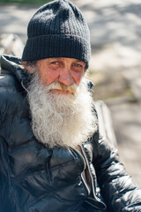 homeless person. Man with white beard sitting on street wearing a black beanie hat © andrey