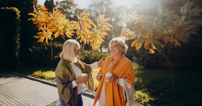 Senior women friends enjoying coffee, conversation in park