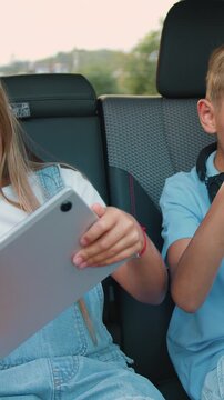 Beautiful children boy and girl having fun playing games on phone and tablet while sitting in a modern car. Little brother and sister are laughing and happily celebrating vin in online game by giving