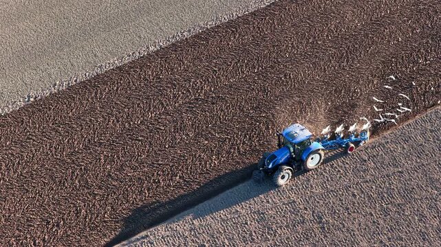 Tractor cultivating the soil for planting crops during a sunny and dry springtime day. Aerial view drone footage from directly above.