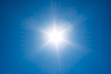 Brilliant sunburst with symmetrical light rays shining against a clear blue sky during an intense summer heat wave © Octavian