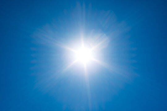 Brilliant sunburst with symmetrical light rays shining against a clear blue sky during an intense summer heat wave