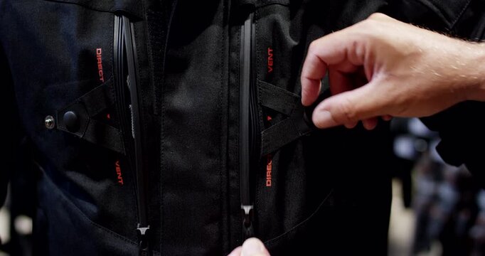Close up of hands opening the ventilation zippers on a black technical motorcycle jacket