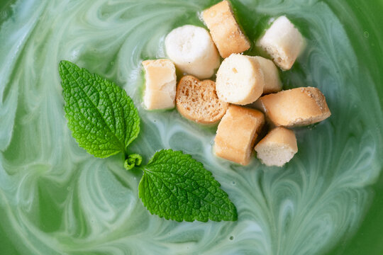 Close up of a bowl of mint or nettle leaves green soup sits on a wooden table. The soup is swirled with cream and topped with croutons. top view. Healthy food