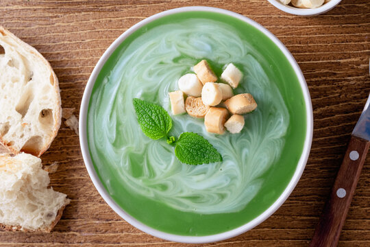 Close up of a bowl of mint or nettle leaves green soup sits on a wooden table. The soup is swirled with cream and topped with croutons. top view. top view. Healthy food