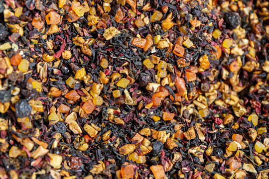 Dry mixture of black loose leaf tea with pieces of dried fruits and berries close up.