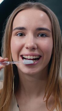 Good-looking 20 years old girl brushing teeth for morning routine and body care.in bathroom at home. Face portrait of happy young woman holding toothbrush brushing teeth looking in camera. Slow motion