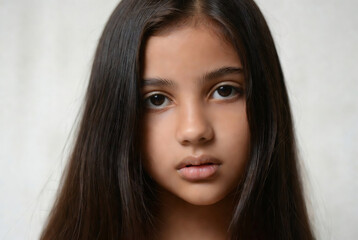 Naklejka premium A young girl with dark hair and brown eyes is looking directly at the camera. She appears to be posing for a portrait in a studio setting.