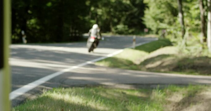Motorcyclist riding a black sport motorcycle through a sharp curve on a rural forest road in summer