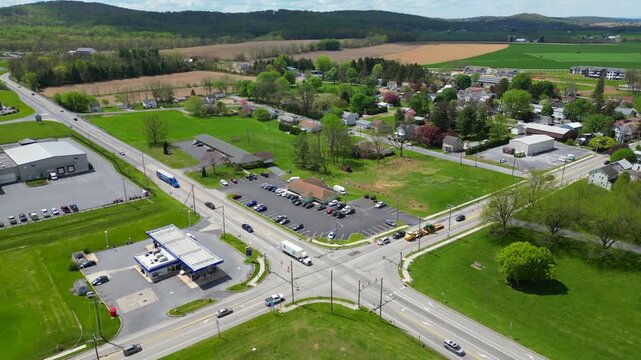 High-angle drone footage capturing a paved road junction situated next to a modern commercial facility, surrounded by lush green trees and manicured lawns.