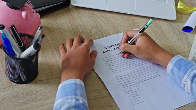 Overhead view of student filling out scholarship application form at desk with piggy bank