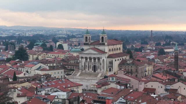 Aerial drone footage featuring a smooth telephoto approach with a slight orbit from the right toward the Duomo di San Pietro Apostolo in Schio, Italy, under a cloudy sunset sky