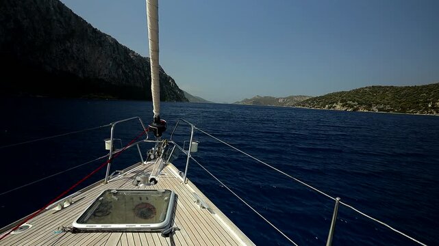 Bowsprit and hatch in the deck of a sailing yacht sailing in a narrow strait between rocky shores
