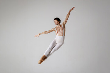 Fototapeta premium Graceful male ballet dancer in mid-air leap on grey background, classical ballet pose