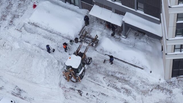 Snow removal in residential yard with tractor and workers, clearing area after snowfall, winter urban maintenance