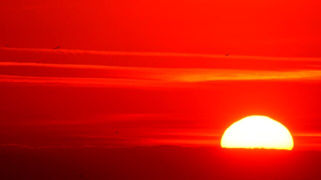 Sunset, sky, red hot sun setting behind vibrant cloud layer in extreme zoom abstract view