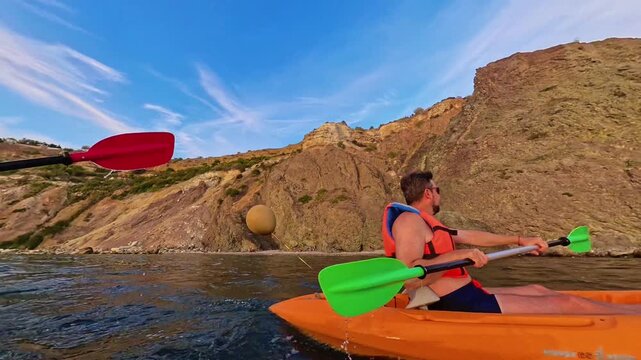 Kayak paddling ocean man in a life jacket navigates an orange boat along a scenic rocky coastline under a bright blue sky