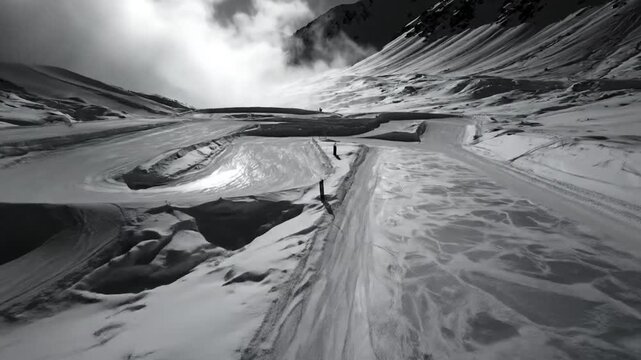 Black and white aerial view of a winding snow track in the mountains with overcast sky