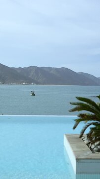 Infinity Pool Edge With Palm Fronds, Persian Gulf Water Meeting Distant Bay And Mountains, Small Boat On Horizon Creating Luxe Travel And Resort Panorama For Cinematic Footage