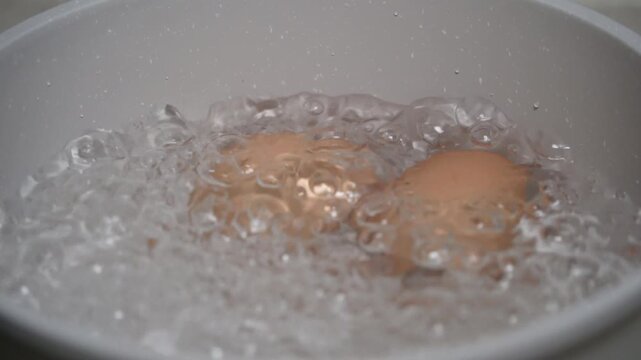 Two chicken egg boiling in pan. Close up of bubbling water while boiling eggs