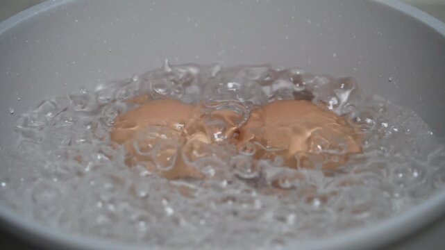 Slow motion of two chicken egg boiling in pan. Close up of bubbling water while boiling eggs