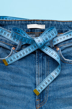 Close-up of blue tape measure used as waistband on blue jeans. Concept of dieting, weight loss, anorexia, obesity, fitness. Measuring tape for tracking body measurements