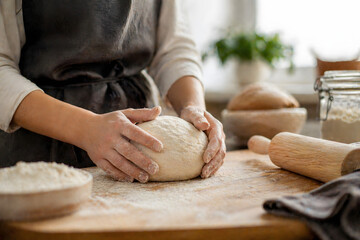 Fototapeta premium Hands kneading fresh dough on wooden table in home kitchen