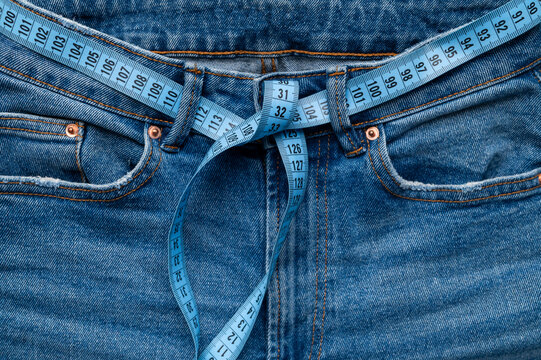 Close-up of blue tape measure used as waistband on blue jeans. Concept of dieting, weight loss, anorexia, obesity, fitness. Measuring tape for tracking body measurements