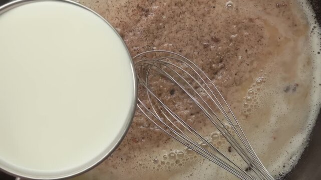 Milk being poured into flour browned in butter on a skillet. Cooking creamy homemade bechamel sauce step by step.
