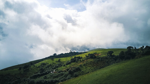 Aerial view of majestic verdant hills bathed in dramatic light, with soft, ethereal clouds drifting above, Obudu, Cross River, Nigeria.