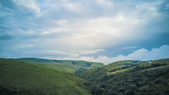 Aerial view of undulating green hills and valleys beneath a dramatic sky, contrasting lush earth with soft, expansive clouds, Obudu, Cross River, Nigeria.