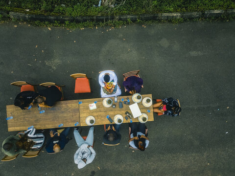 Aerial view of a group sharing a vibrant meal at a long wooden table on a dark asphalt road, Obudu, Cross River, Nigeria.
