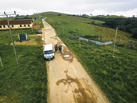 Aerial view of a winding dirt road, contrasting verdant hills and a building, with a white van and people, Obudu, Cross River, Nigeria.