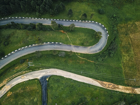 Aerial view of a dramatic winding road, its white barriers contrasting sharply with the vibrant green hills and dark forest, Obudu, Cross River, Nigeria.