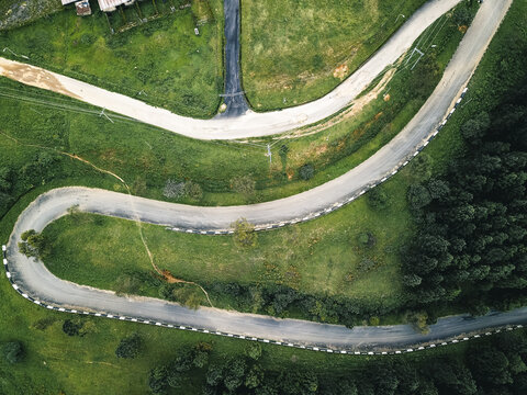 Aerial view of a dramatic serpentine road winding through lush green hills and dark forests, marked by contrasting white edges, Obudu, Cross River, Nigeria.