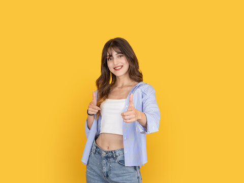 Smiling young woman pointing forward with finger guns in playful gesture, expressing confidence and positive attitude. Isolated on bright yellow background with copy space for advertising use.