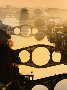 Aerial view of stone bridges and a pagoda silhouetted against golden reflective waters, Hu Zhou Shi, Zhe Jiang Sheng, China.
