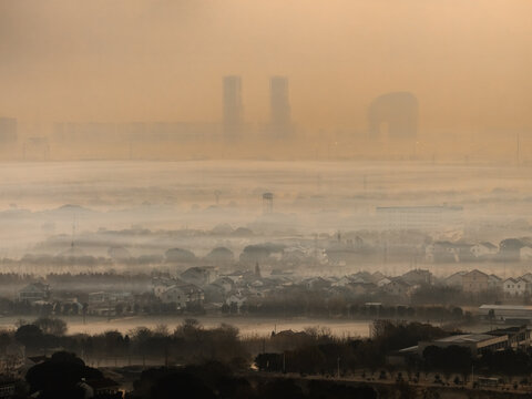 Aerial view of a city shrouded in a thick, golden-brown haze, with distant modern towers barely visible above the murky fog, Hu Zhou Shi, Zhe Jiang Sheng, China.