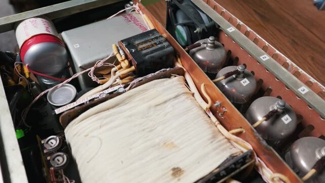 Internal components of a custom-built tube amplifier are shown in detail. Retro radio tubes, capacitors, and a cooling fan sit within the metal chassis. The scene captures DIY electronics craft